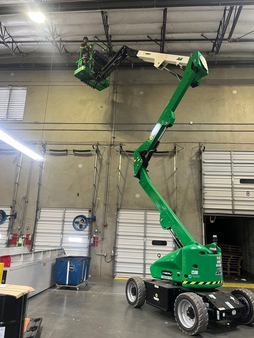 Technician on a boom lift performing overhead low voltage installation in a warehouse